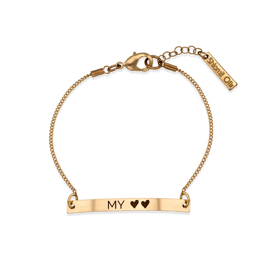 Finished flat-lay image of a fine gold chain bracelet with an engraved bar reading MY and two hearts, with lobster clasp and tag, on white, photographed and retouched in the course.