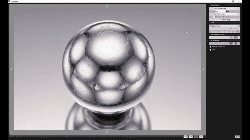 A polished chrome sphere photographed tethered during the Lighting the Metal Sphere lesson: the reflections on its surface show the lights and panels placed around the set.