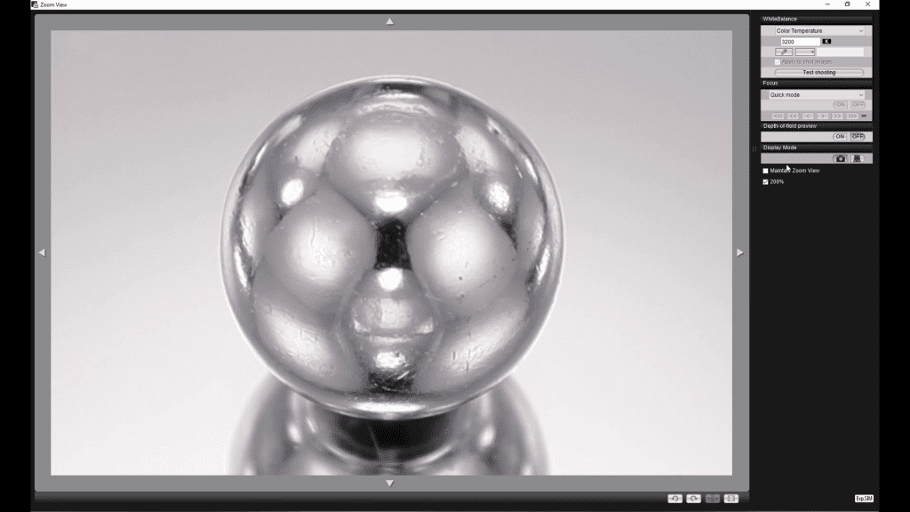 A polished chrome sphere on a white surface captured tethered during the Lighting the Metal Sphere lesson: the broad bright reflection of a panel above and the dark reflections of cards around the set are visible on its surface.